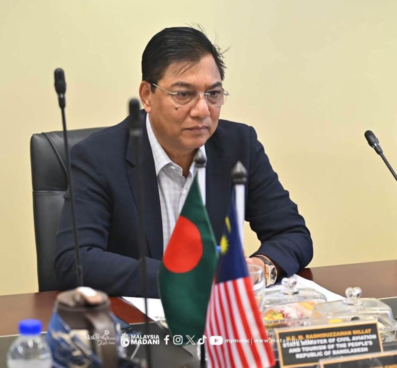 M. Rashiduzzaman Millat at a meeting with Bangladesh and Malaysia flags; original photograph attribution retained